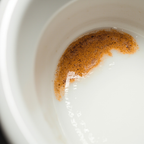 Close-up of orange iron stain ring on white porcelain toilet bowl at the waterline